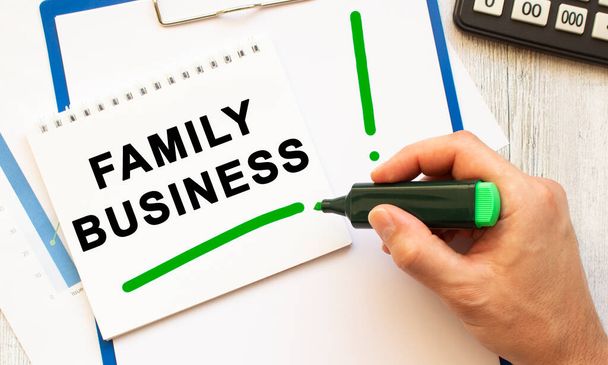 A hand with a marker writes the text FAMILY BUSINESS in a notebook on the desktop. View from above. Business concept. - Photo, Image