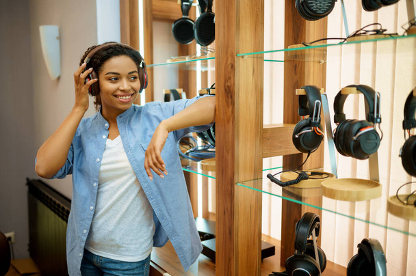 Young woman listening to music in headphones store. Female person in audio shop, showcase with earphones on background, buyer in the multimedia salon - Photo, Image