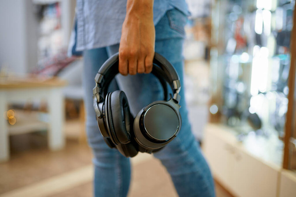 Woman buying headphones in audio store, music fan. Female person in music shop, showcase with earphones on background, buyer in multimedia salon - Photo, Image
