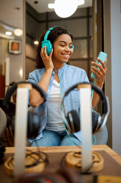 Egy nő zenét hallgat a fülhallgatóban. Nő személy audio shop, kirakat fülhallgató a háttérben, vevő a multimédia szalonban - Fotó, kép