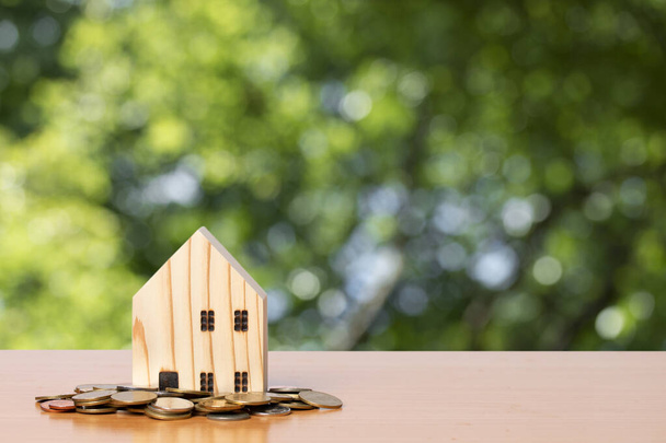 Κέρμα χρημάτων με ένα ξύλινο μοντέλο σπιτιού σε φόντο πράσινο φύλλο θαμπάδα. έννοια για την αγορά κατοικίας. - Φωτογραφία, εικόνα
