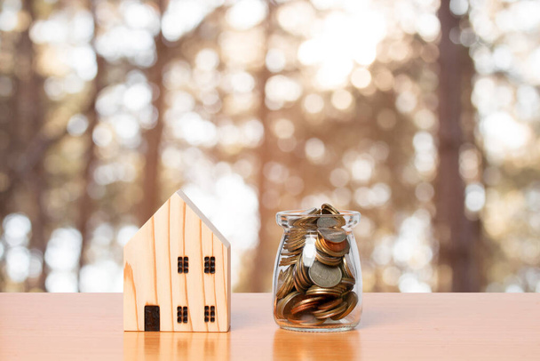 木製のホームモデルと瓶のガラスでお金のコインの節約。家を買うという考え方は - 写真・画像