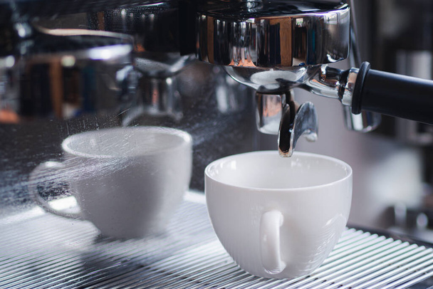 Κοντινό πλάνο ενός portafilter με ένα λευκό φλιτζάνι καφέ σε μια καφετιέρα σε ένα καφέ κατάστημα. Η διαδικασία της παρασκευής καφέ βήμα προς βήμα. Έννοια των ποτών. - Φωτογραφία, εικόνα