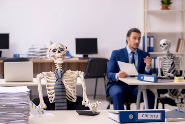 Młody pracownik płci męskiej ze szkieletami w biurze - Zdjęcie, obraz