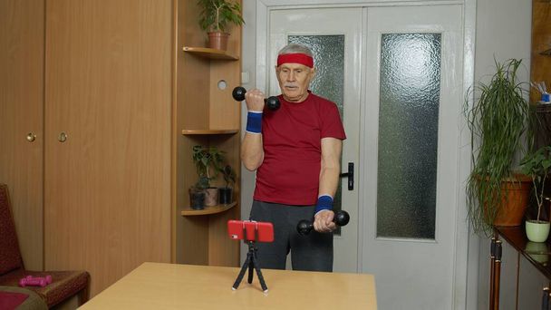 Viejo abuelo mayor haciendo ejercicio con pesas, entrenamiento, fitness, actividad deportiva en casa - Foto, imagen
