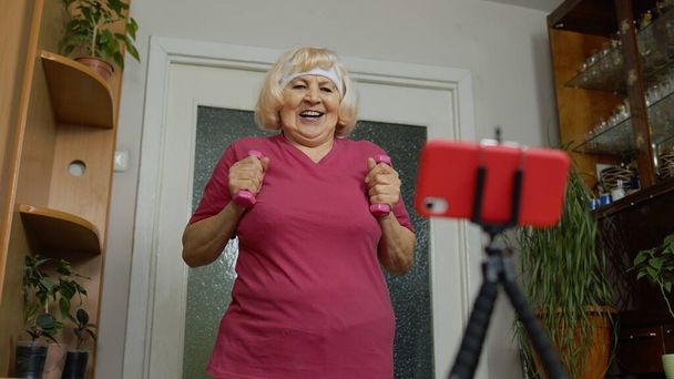Oude grootmoeder vrouw doet workout met halters, training, fitness, sport activiteit thuis - Foto, afbeelding