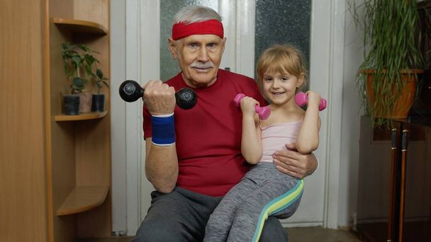 Dziecko dziewczynka z dziadkiem w odzieży sportowej podejmowania ćwiczeń sportowych z hantlami - Zdjęcie, obraz