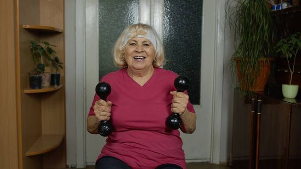 Ηλικιωμένη γιαγιά γυναίκα που κάνει ασκήσεις άρσης βαρών γυμναστήρια αλτήρες άσκηση στο σπίτι - Φωτογραφία, εικόνα