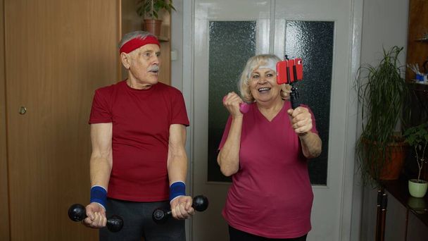 Senioren-Paar beobachtet Online-Workout-Übungen auf Handy und Training mit Kurzhanteln - Foto, Bild