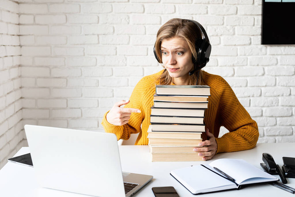Dálkové studium. E-learning. Mladá žena v černých sluchátkách pomocí notebooku drží hromadu knih - Fotografie, Obrázek