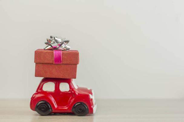 A red retro toy car delivers a gift box for a holiday on a light background. - Fotografie, Obrázek