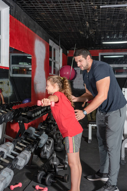 Az edző együtt dolgozik a lánnyal az edzőteremben, és megmutatja, hogyan kell helyesen csinálni a gyakorlatot.. - Fotó, kép