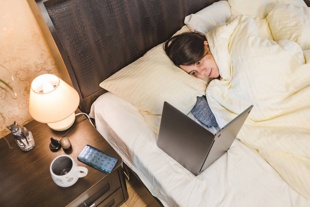 mujer acostada en la cama cubierta con manta mirando espectáculo en el espacio de copia portátil - Foto, imagen