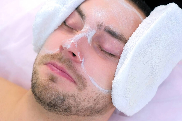 Cosmetologist wipes moisturizing mask from mans face using terry mittens. - Photo, image