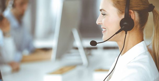 Blonde business woman using headset for communication and consulting people at customer service office. Call center. Group of operators at work - Foto, Imagem