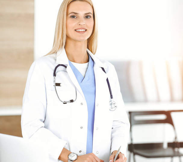 Doctor woman controls medication history records and exam results while using clipboard in sunny hospital . Medicine and healthcare concept - Photo, Image