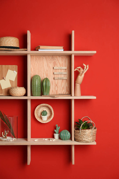 Stylish wooden shelves with decorative elements on red wall - 写真・画像