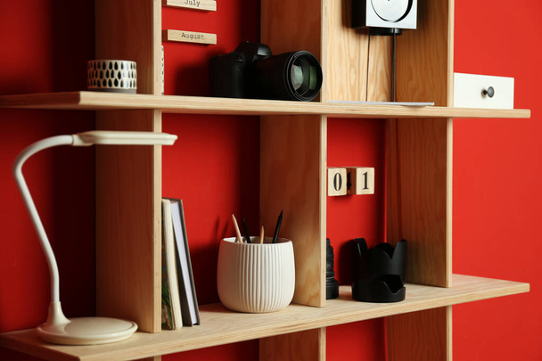Stylish wooden shelves with photography equipment and decorative elements on red wall - Foto, imagen