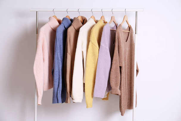 Warm sweaters hanging on rack against white background - Фото, изображение