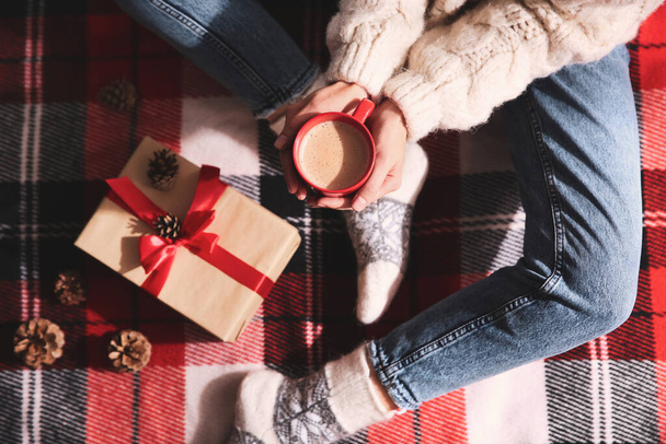 Woman relaxing with cup of hot winter drink on checkered plaid, top view - 写真・画像