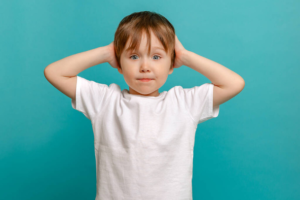 Ein vier- oder fünfjähriges Kind, das sich die Hände vors Gesicht hält, staunt auf grünem Hintergrund. Emotionaler Junge posiert für die Kamera - Foto, Bild