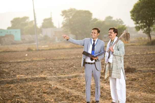 Businessman checking file and discussing with farmer on agriculture field - 写真・画像