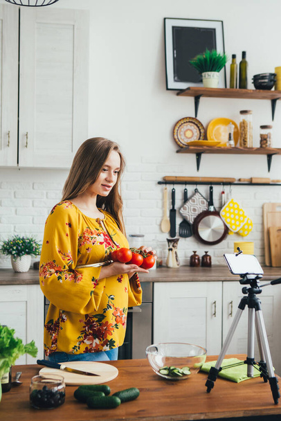 Young pretty pregnant girl blogger shoots a video of a salad recipe on a smartphone camera. The concept of healthy eating. Toning. - 写真・画像