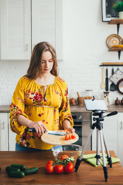 Young pretty pregnant girl blogger shoots a video of a salad recipe on a smartphone camera. The concept of healthy eating. Toning. - Zdjęcie, obraz