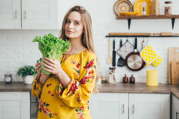 Young cute pregnant girl preparing vegetable salad in the kitchen. The concept of healthy eating. Toning. - Foto, afbeelding