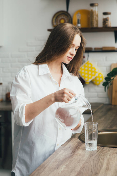 Young cute pregnant girl drinking clean water in the kitchen. The concept of a healthy lifestyle. Toning. - Foto, Bild
