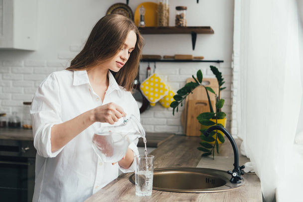 Young cute pregnant girl drinking clean water in the kitchen. The concept of a healthy lifestyle. Toning. - Foto, Imagem