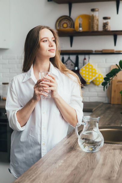 Young cute pregnant girl drinking clean water in the kitchen. The concept of a healthy lifestyle. Toning. - Fotografie, Obrázek