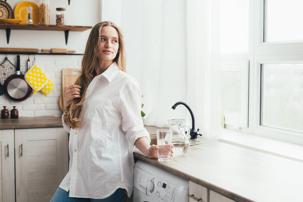 Young cute pregnant girl drinking clean water in the kitchen. The concept of a healthy lifestyle. Toning. - Fotoğraf, Görsel