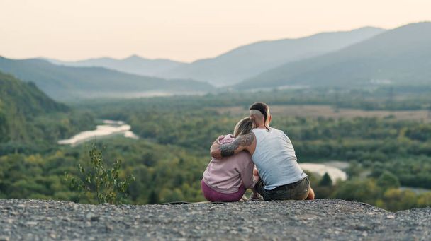 Young man hugs his girlfriend on the mountain peak at sunset background. - Valokuva, kuva