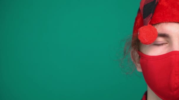 Портрет мальчика в шляпе Санты носит красную медицинскую маску, смотрит в камеру - Кадры, видео