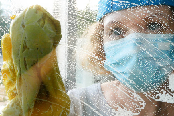 Γυναίκα με προστατευτική μάσκα και γάντια πλύσιμο παραθύρων. Έννοια υπηρεσιών καθαρισμού παραθύρων - Φωτογραφία, εικόνα