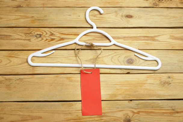 Kleiderbügel und leeres rotes Preisschild auf hölzernem Hintergrund, Bekleidungsverkauf, Nahaufnahme - Foto, Bild