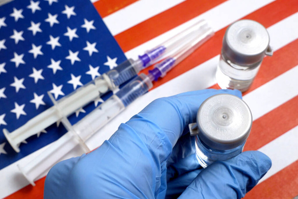 flacone un vaccino è tenuto a mano in un guanto sullo sfondo della bandiera USA, vaccino contro il coronavirus, primo piano - Foto, immagini