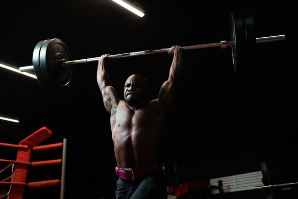 Heavyweight man training with a barbell. Bodybuilding trainer lifts heavy weights in the gym, preparing for competition - Foto, imagen