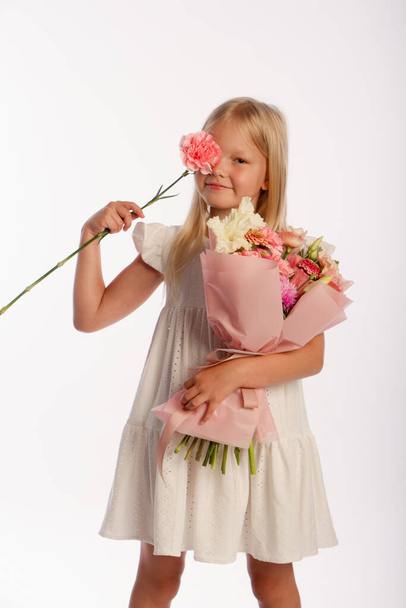 Studio portrait of cute blonde girl in white dress with beautiful gift bouquet, white background, selective focus - Photo, image