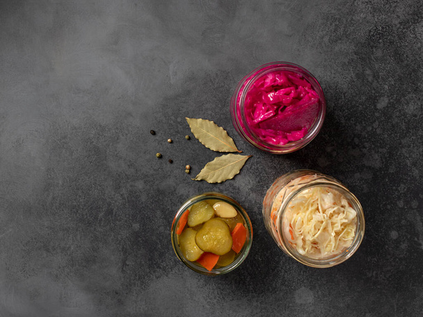 assortment of fermented vegetables: cabbage, cucumbers, carrots, in glass jars. dark concrete background, top view, copy space - 写真・画像