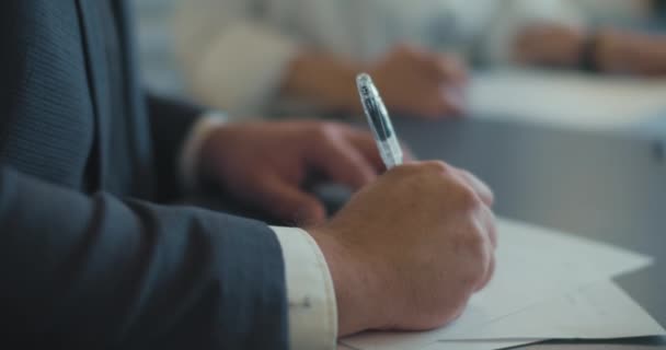 Primer plano de las manos de un hombre de negocios escribiendo algo en un documento durante una reunión de negocios. Movimiento lento - Imágenes, Vídeo