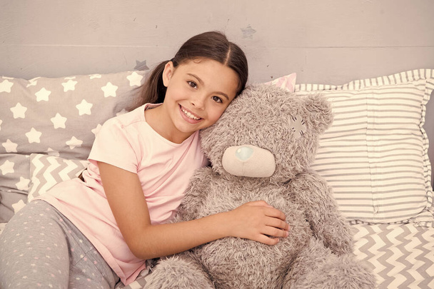 Pure love concept. Kids evening routines. Favorite toy. Girl child hug teddy bear in her bedroom. Pleasant time in cozy bedroom. Girl kid long hair cute pajamas relax and play plush teddy bear toy - Photo, image
