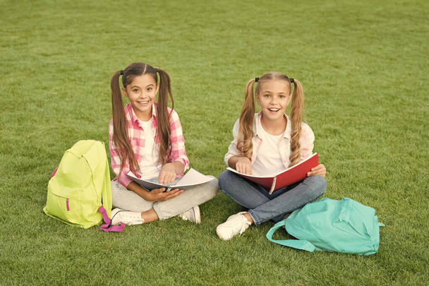 Playful girls. literature for girls. do homework together. find something interesting in book. making notes. spend free time after school. small kid friends relax on grass. back to school - Фото, изображение