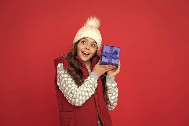 Xmas gift idea. Winter holidays. Happy kid in winter outfit hold gift box red background. Wish list. Holidays season. Happy childhood. Christmas gifts. Vacation souvenirs concept. Gift for female - Photo, image