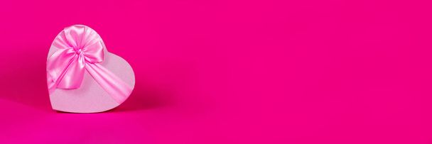 Бэйнер. День Святого Валентина. Розовая коробка сердца с луком на розовом фоне. Подарочное сердце. Любовь и страсть. Подарок на День Святого Валентина. Принято. День Матери. Вид сверху. - Фото, изображение