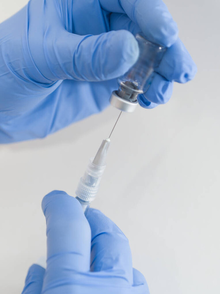 Hands in Blue Rubber Gloves Holding Medical Syringe and Vial Closeup on White Background - Foto, afbeelding