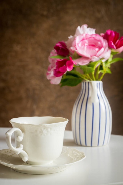 a stylish cup standing on the table and a jug with a bouquet of flowers - Foto, imagen