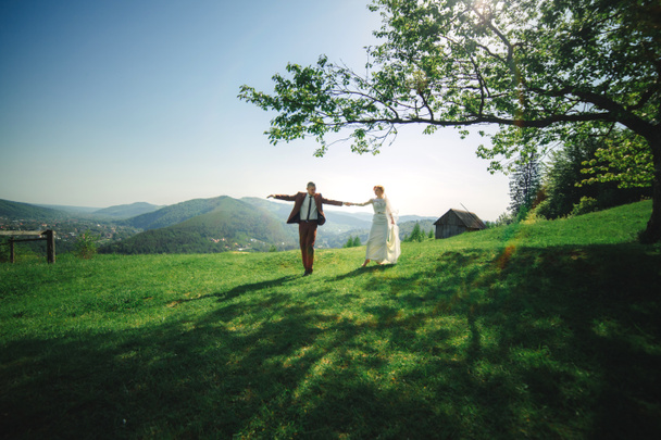 happy stylish bride and groom running and having fun in mountains on summer sunny day. gorgeous newlywed couple laughing, true feelings. emotional romantic moment - Foto, immagini