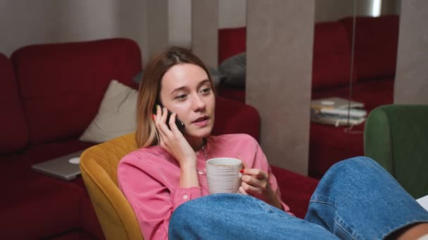 Entspannte Frau, die zu Hause in Zeitlupe mit dem Handy spricht. Lächelndes Mädchen im Smartphone-Gespräch auf der Couch zu Hause. - Filmmaterial, Video